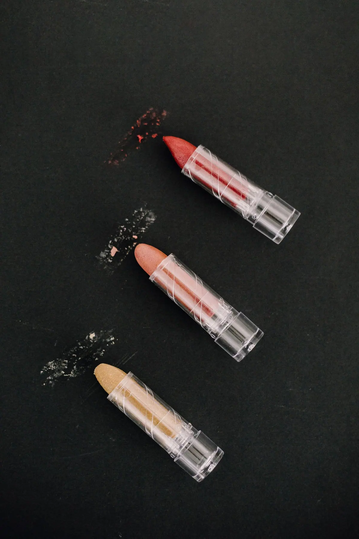 Drei Schokolade-Lippenstifte mit Glitzerspur auf schwarzem Grund
