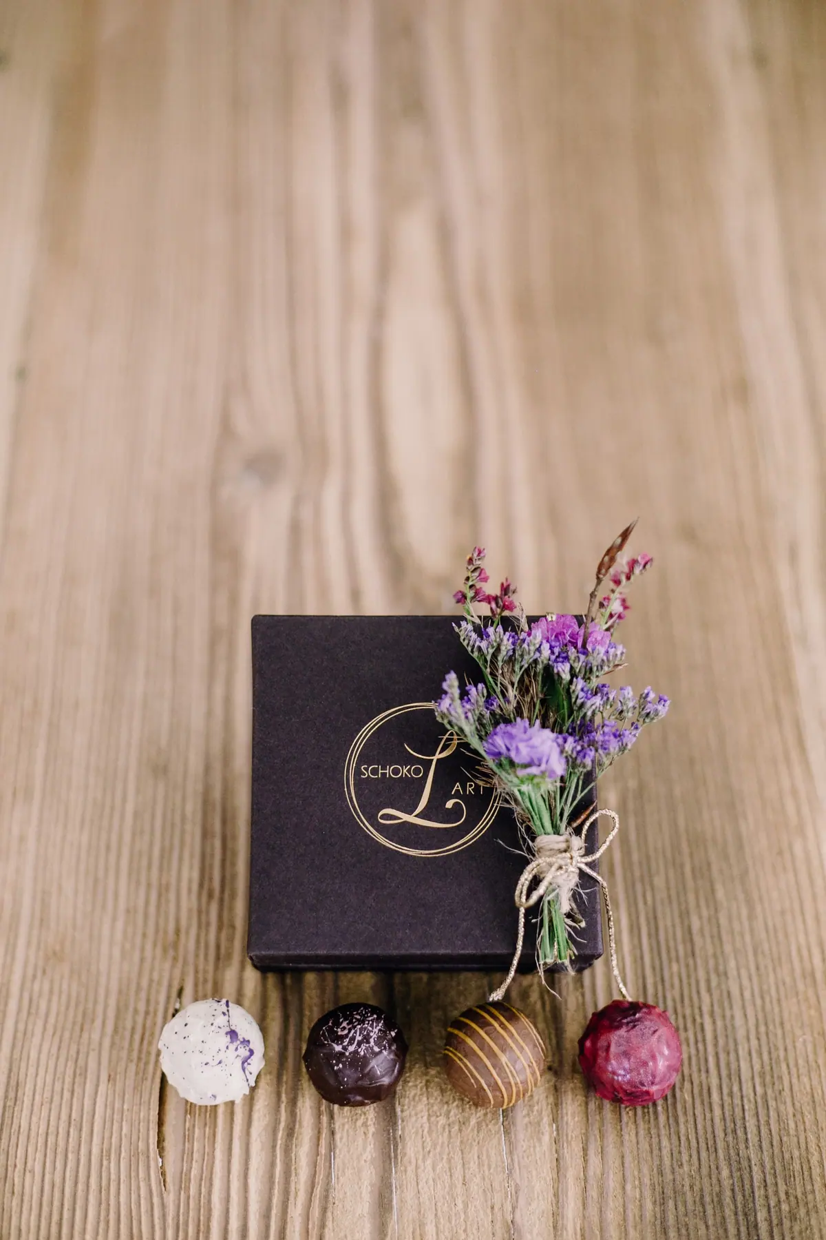 Schwarze Geschenkschachtel mit Lavendel und vier Pralinen auf Holz
