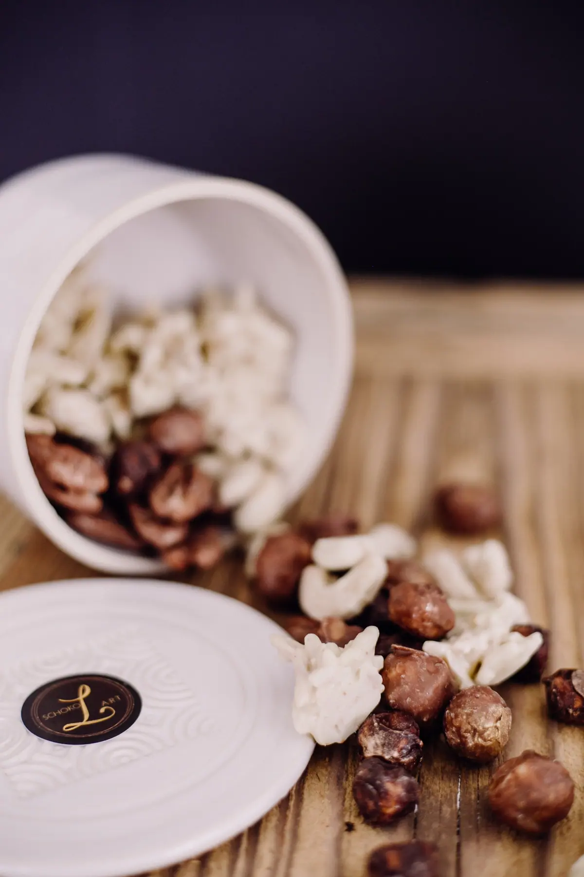 Umgekippte Keramikdose mit schokolierten Haselnüssen und weißen Cashews