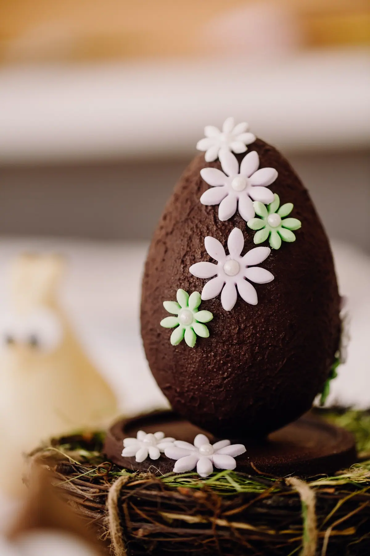 Schokoladen-Osterei mit weißen Zuckerblumen in einem Nest
