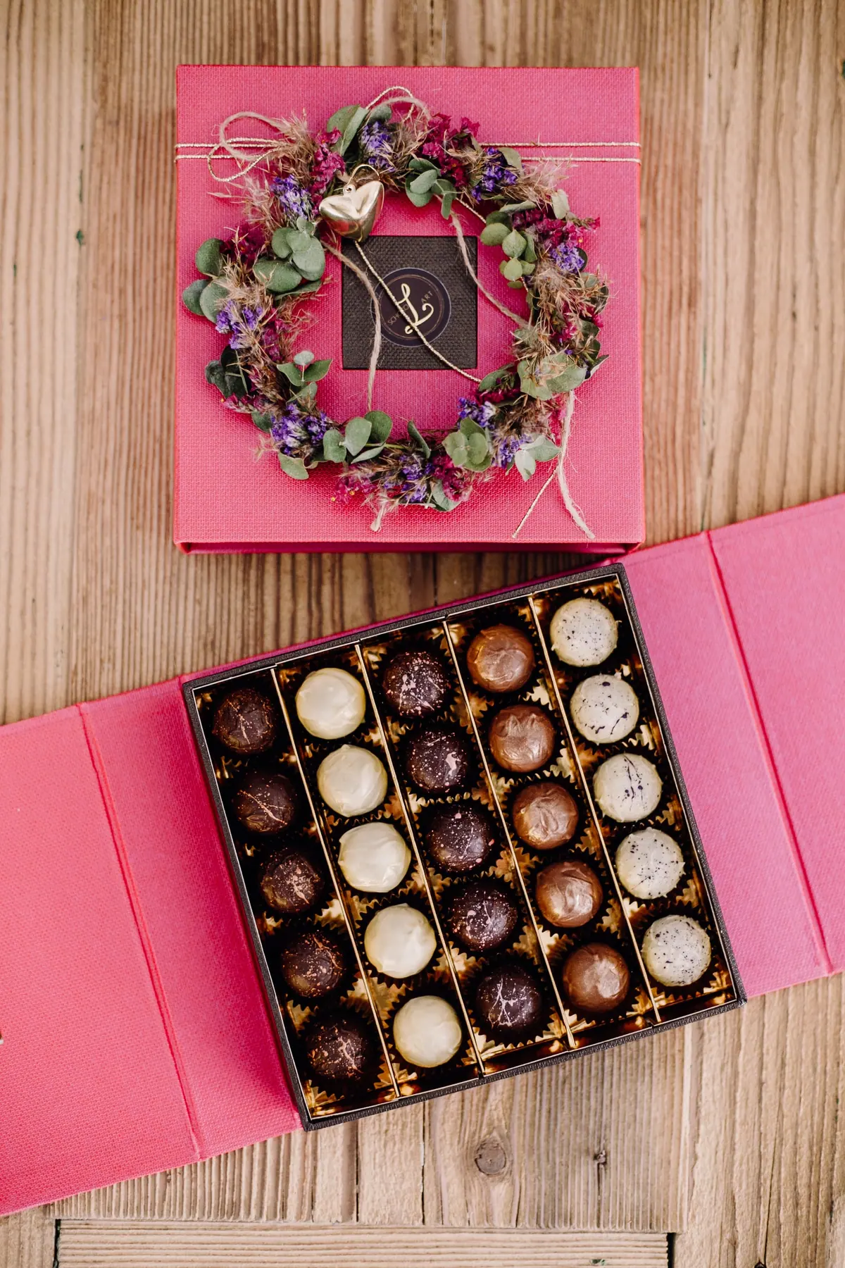Rosa Geschenkbox mit 25 Pralinen, auf dem Deckel ein Blumenkranz um das schokoLart-Logo