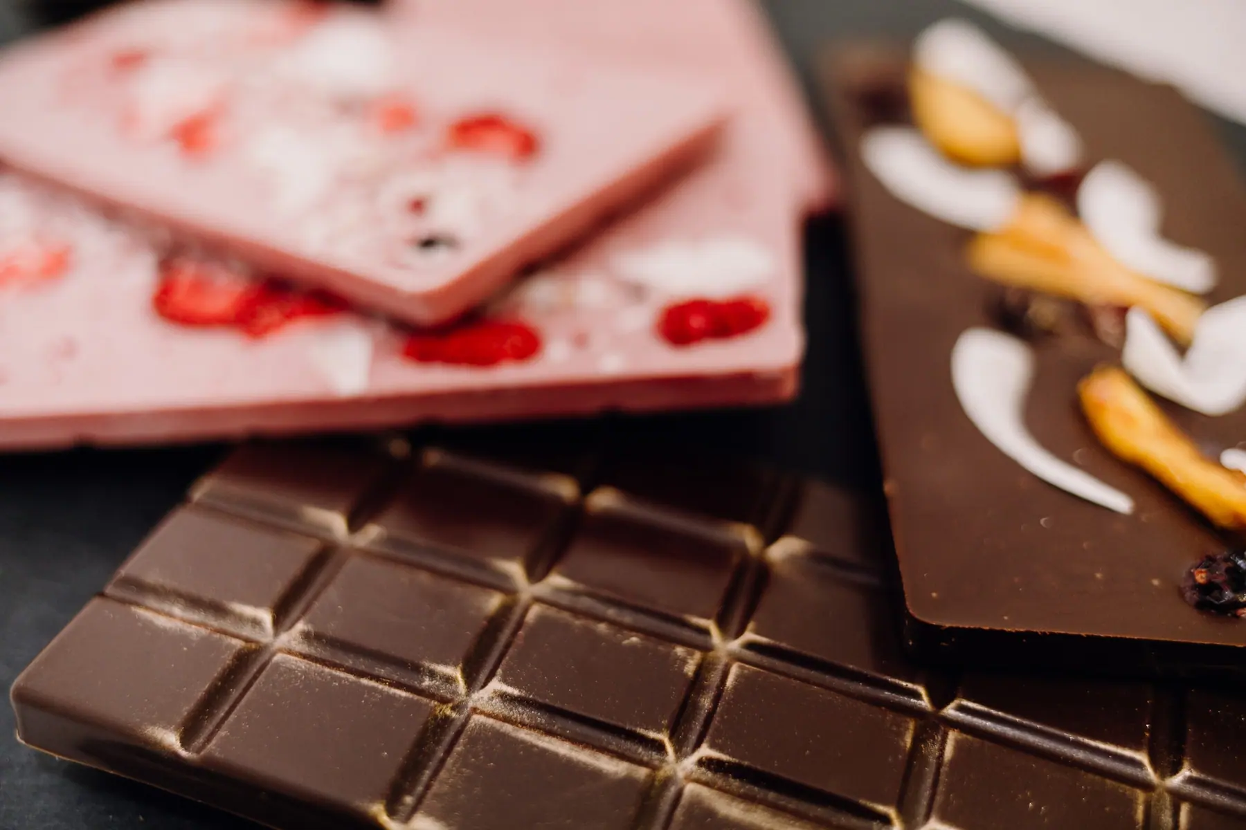 Schokoladetafeln in Rosa, Weiß und Zartbitter mit Erdbeeren und Früchten, übereinander gelegt