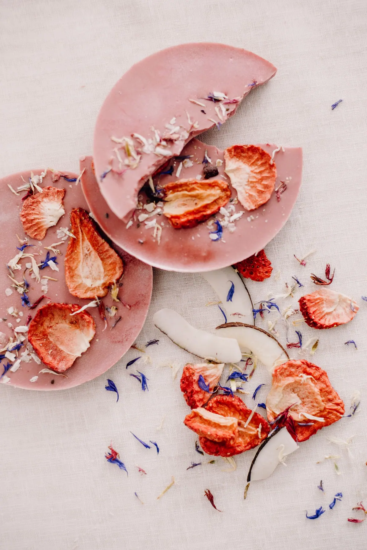 Rosa Schokotaler mit getrockneten Erdbeeren und Kornblumen, einer davon gebrochen