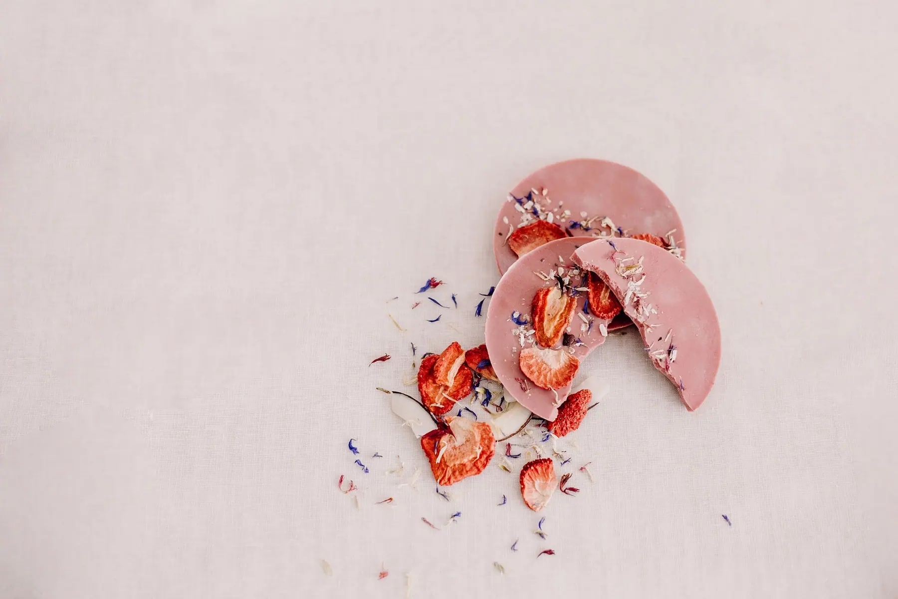 Zwei rosa Schokotaler mit getrockneten Erdbeeren und Blütenblättern auf hellem Grund