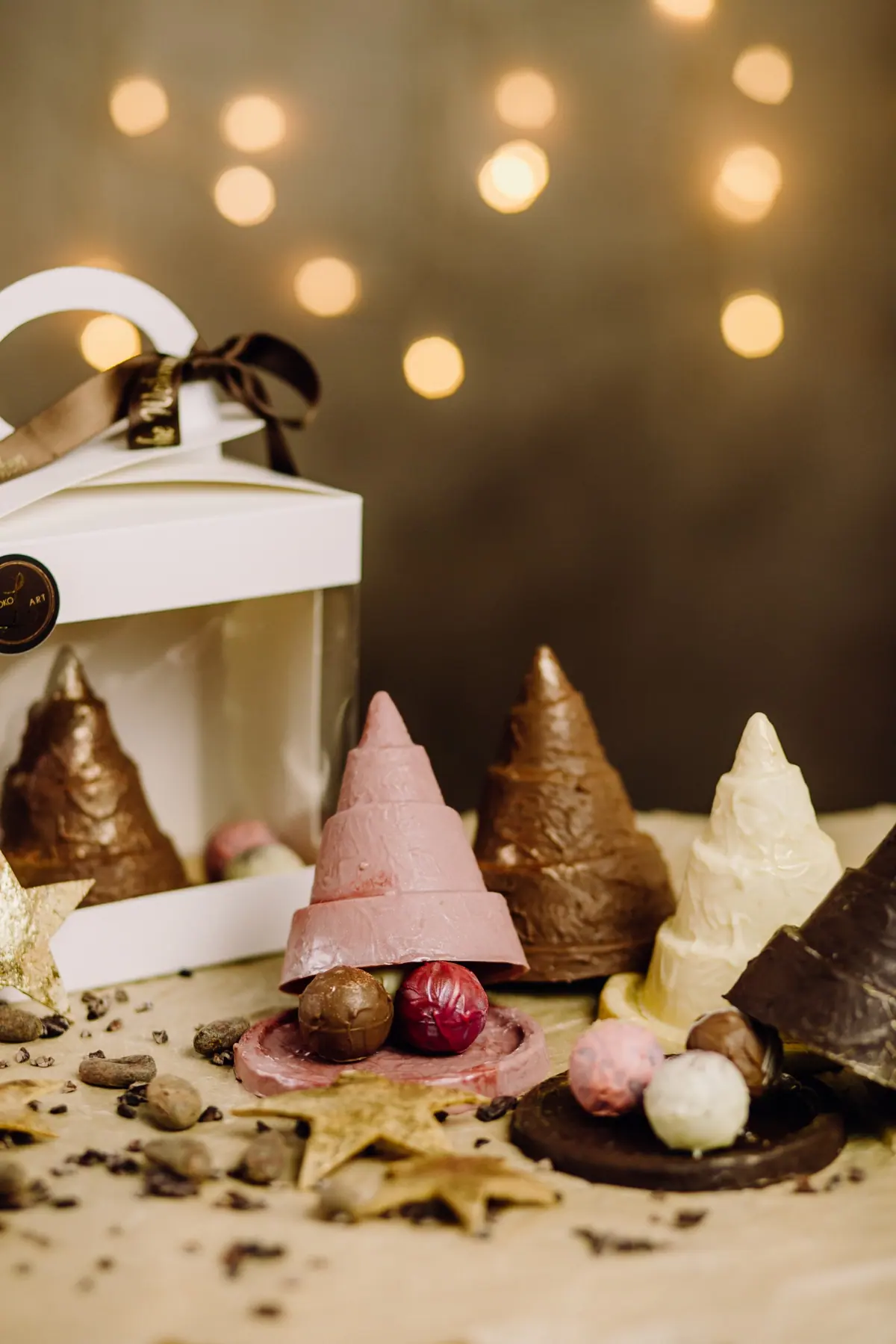 Christbäume aus weißer, rosa und dunkler Schokolade vor Lichterglanz