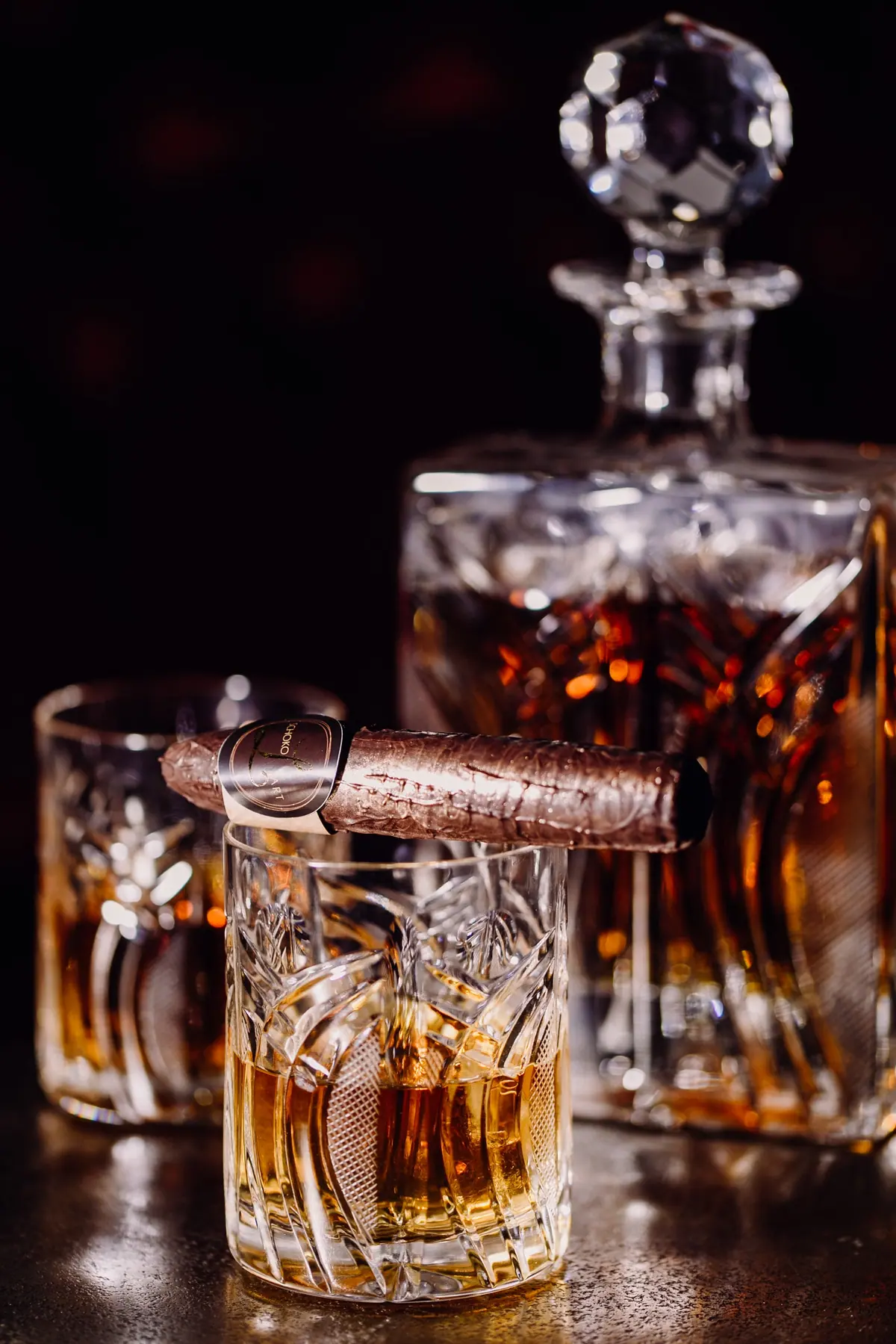 Zigarre aus Schokolade auf einem Whiskyglas, dahinter eine Kristallkaraffe