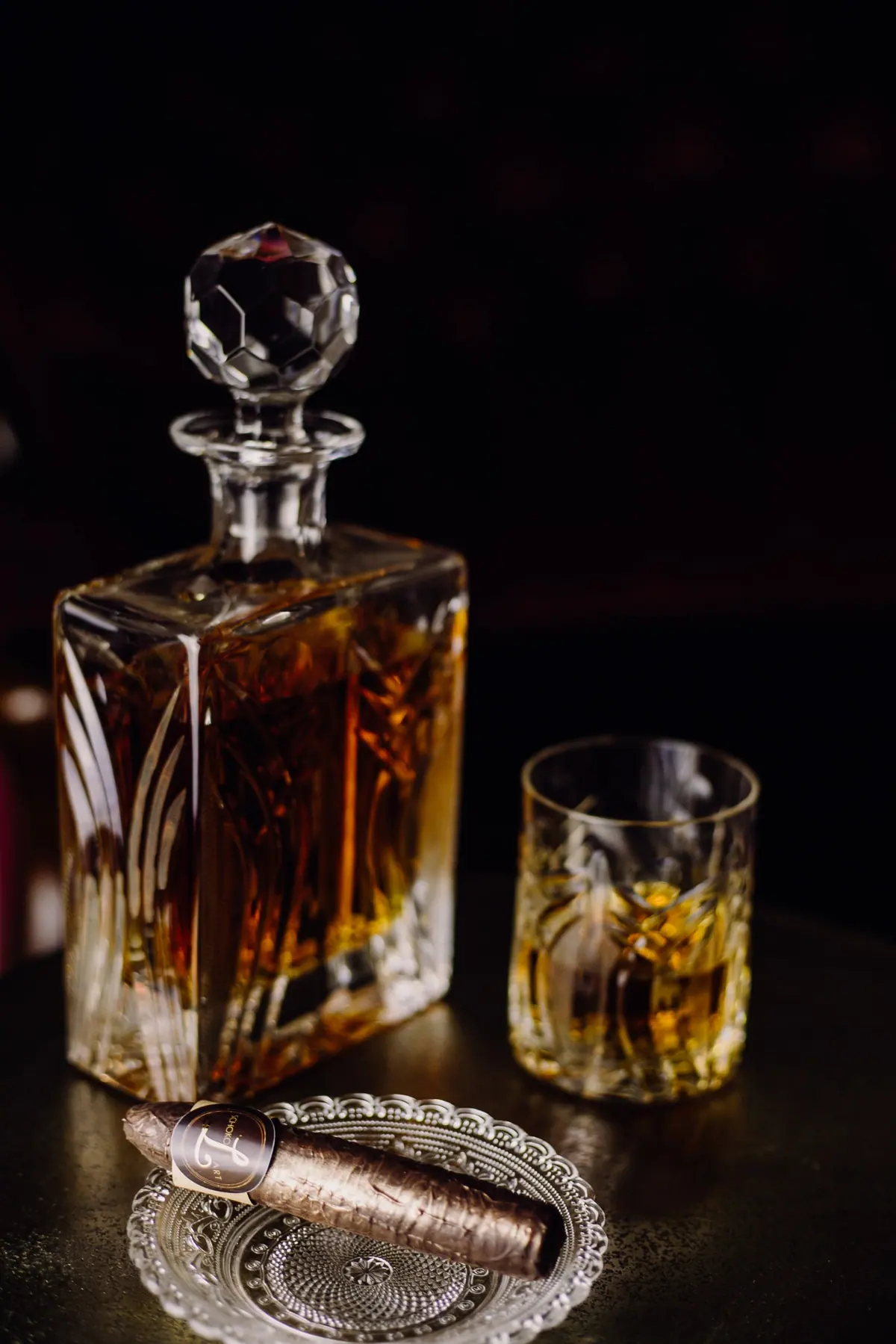 Einzelne Schokozigarre auf einem Kristallteller neben Whiskykaraffe und Glas